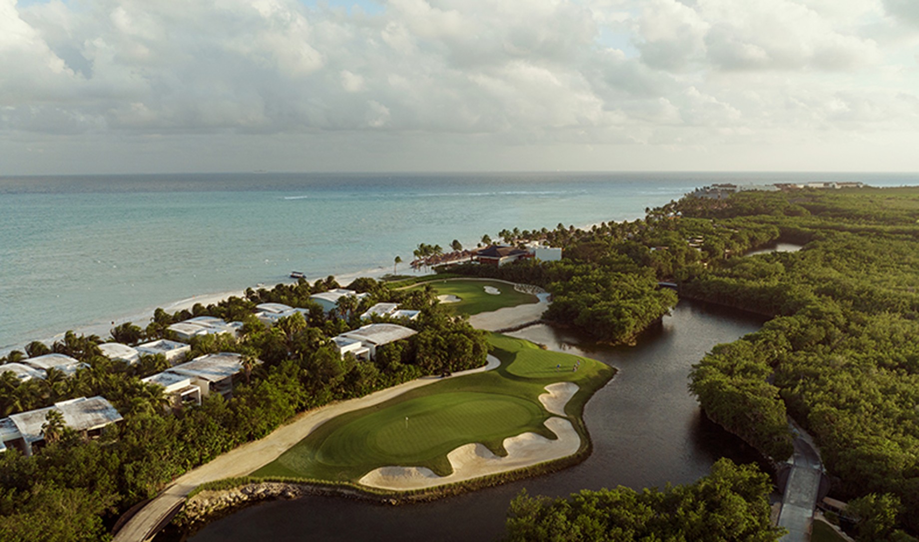 Toma aérea de villas de lujo y fairway del campo de golf El Camaleón Mayakoba integrados en la selva y costa del Caribe mexicano.