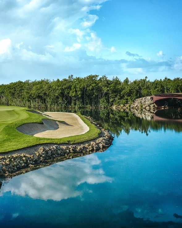 Búnker de arena y canal de agua cristalina en el campo de golf El Camaleón Mayakoba, reflejando el cielo y la selva de la Riviera Maya.